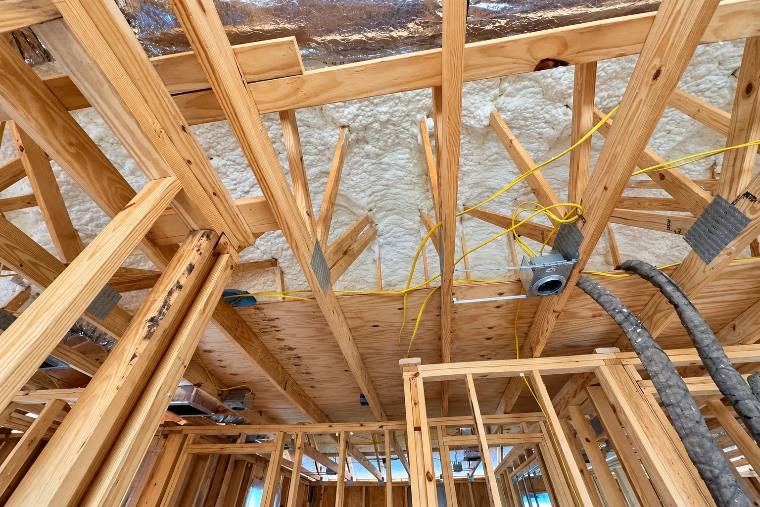 Exposed roof framing with foam insulation between rafters, yellow wiring, and flexible ducts.