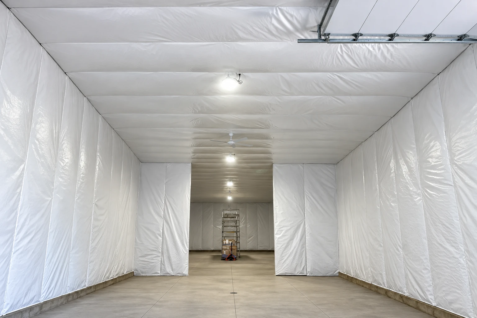 A large commercial room is lined with white insulation panels across its walls and ceiling, with lights and a concrete floor.