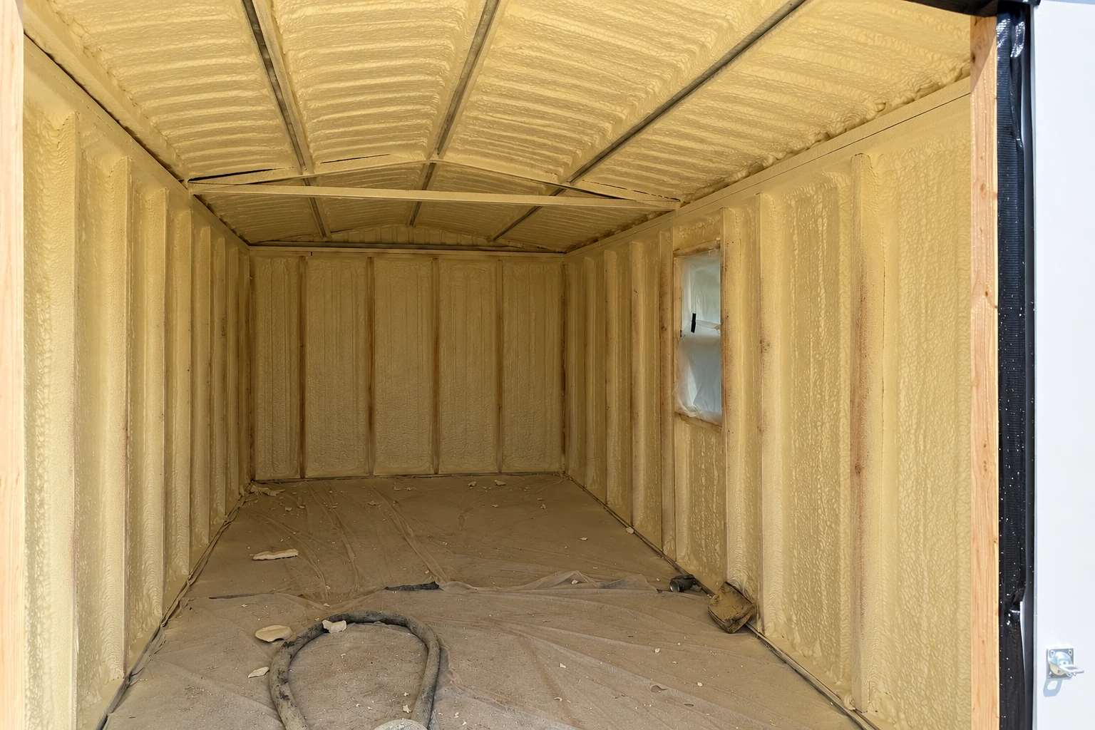 Interior of a framed commercial space with yellow spray foam coating the walls and ceiling.
