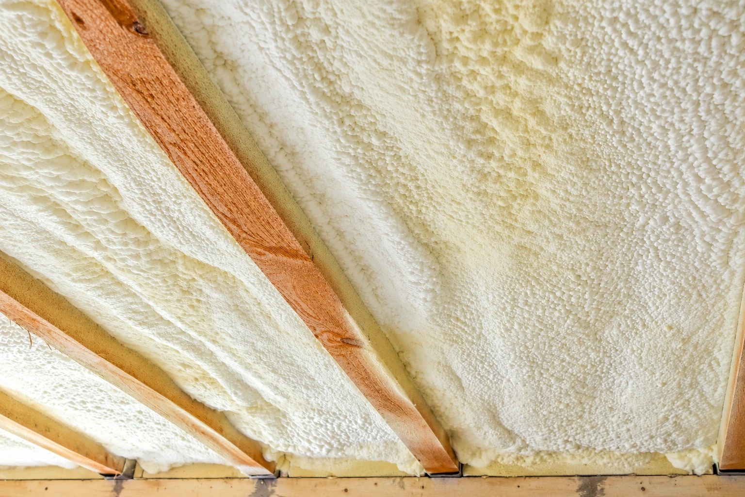 Close view of rough white spray foam insulation filling the spaces between exposed wooden roof rafters.